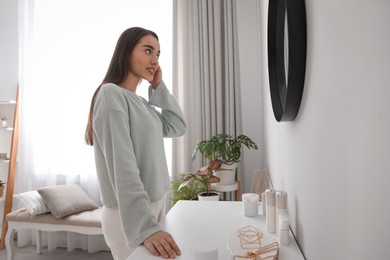 Photo of Young woman doing hair near mirror at home. Morning routine
