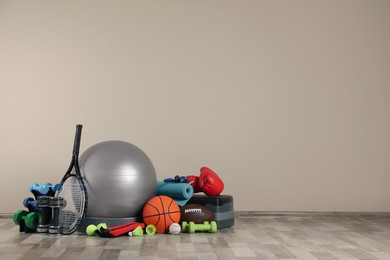 Set of different sports equipment on floor near beige wall, space for text