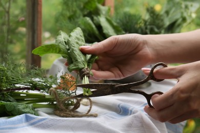 Woman cutting fresh green leaves with scissors indoors, closeup. Drying herbs