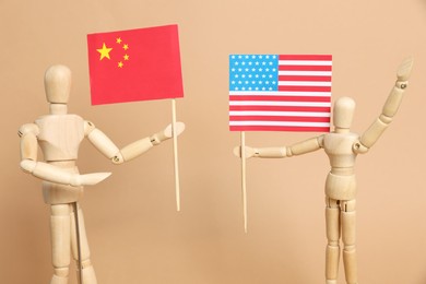 Wooden mannequins holding American and Chinese flags on beige background. Trade war