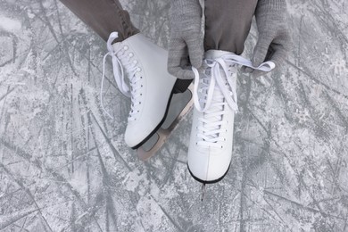 Woman lacing figure skates on ice, top view