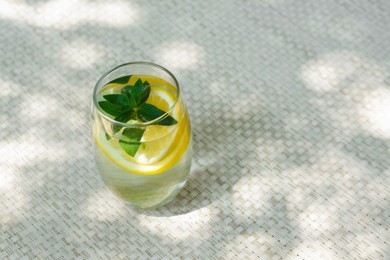 Refreshing water with lemon and mint on wicker mat, space for text