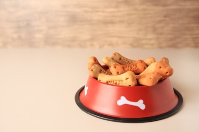 Photo of Bone shaped dog cookies in feeding bowl on beige table, space for text
