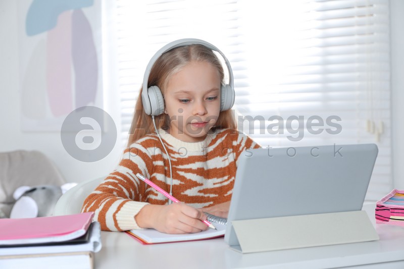 Cute little girl with modern tablet studying online at home. E-learning