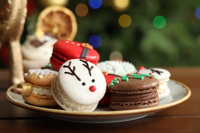 Beautifully decorated Christmas macarons on wooden table against blurred festive lights, closeup