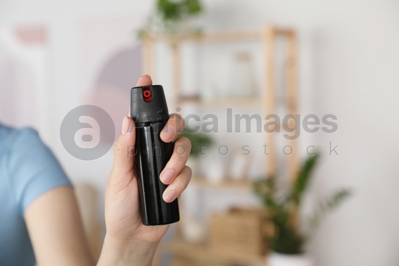 Woman using pepper spray indoors, closeup view