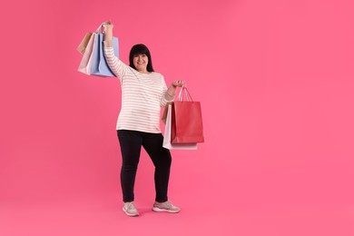 Beautiful overweight mature woman with shopping bags on pink background. Space for text