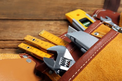 Photo of Belt with utility knife and different tools on wooden table, closeup