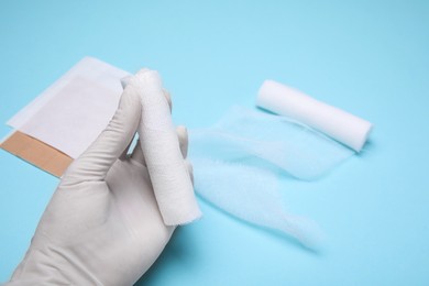 Doctor holding white bandage rolls on light blue background, closeup