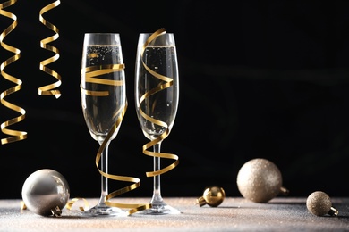 Glasses of champagne, Christmas decor and serpentine streamers on black background. Space for text