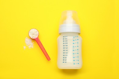 Feeding bottle with infant formula and powder on yellow background, flat lay