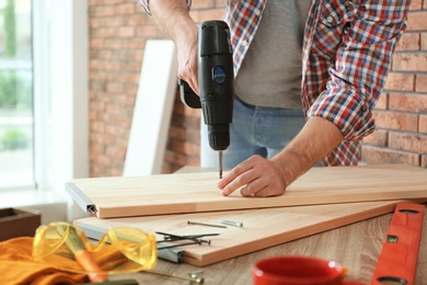 Young man working with electric screwdriver near brick wall