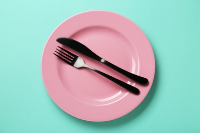 Photo of Pink ceramic plate and cutlery on turquoise background, top view