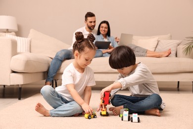 Cute children playing with toys while parents using gadgets on sofa in living room