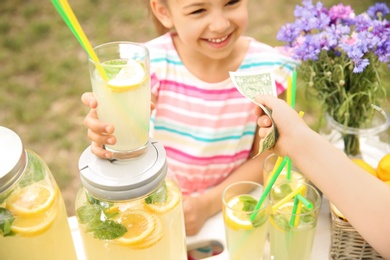 Little girl selling natural lemonade at stand in park