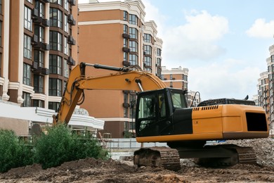 Modern excavator near buildings on construction site