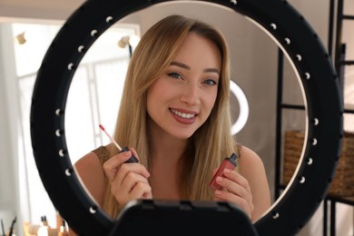 Beautiful young woman with liquid lipstick indoors, view through ring lamp