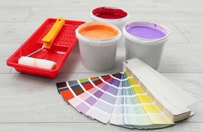 Buckets of paints, palette and decorator's tools on light wooden background
