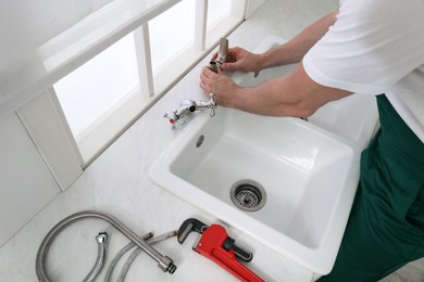 Photo of Professional plumber fixing water tap in kitchen, above view