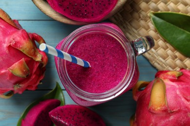 Delicious pitahaya smoothie in mason jar and fresh fruits on light blue wooden table, flat lay