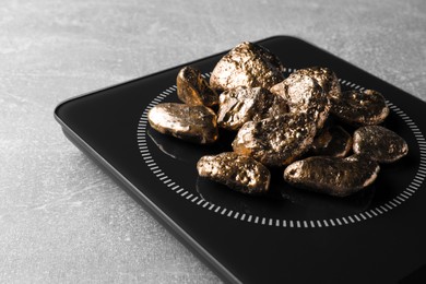 Photo of Digital scales with gold nuggets on light grey table, closeup