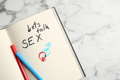 Notebook with phrase "LET'S TALK SEX" and gender symbols on marble background, top view