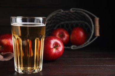 Glass of delicious cider and ripe red apples on wooden table. Space for text