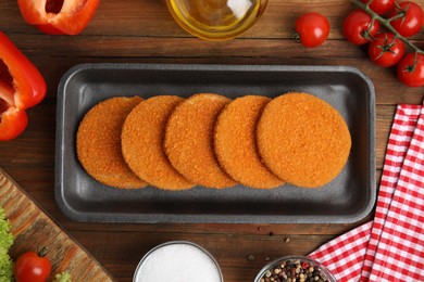 Uncooked breaded cutlets on wooden table, flat lay. Freshly frozen semi-finished product
