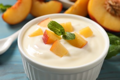 Delicious yogurt with fresh peach and mint on light blue table, closeup