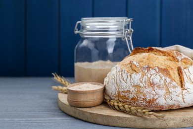 Photo of Freshly baked bread, flour and sourdough on grey wooden table. Space for text