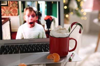 Photo of MYKOLAIV, UKRAINE - DECEMBER 25, 2020: Laptop displaying Home Alone movie indoors, focus on cup of sweet drink and tangerine slices. Cozy winter holidays atmosphere