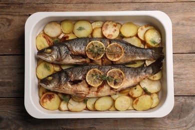 Photo of Baking tray with delicious baked sea bass fish and potatoes on wooden table, top view