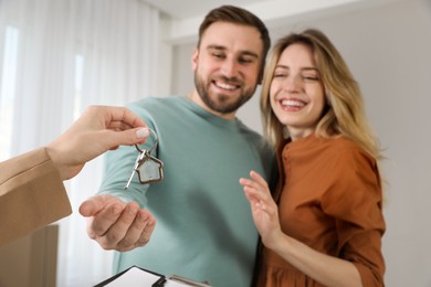 Real estate agent giving key to happy young couple in new house, focus on hands