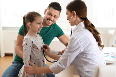 Father and daughter visiting pediatrician. Doctor examining little patient with stethoscope in hospital