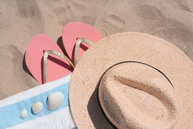 Straw hat, beach towel, seashells and flip flops on sand, flat lay