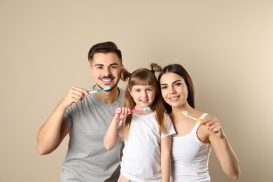 Little girl and her parents brushing teeth together on color background