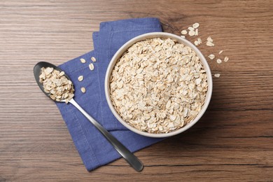 Bowl and spoon with oatmeal on wooden table, flat lay
