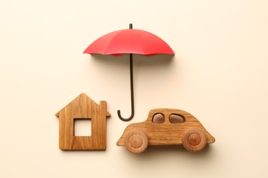 Mini umbrella, house model and toy car on beige background, flat lay