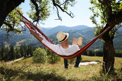Man reading book in hammock outdoors on sunny day