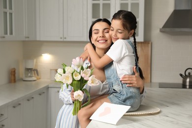 Little daughter congratulating her mom in kitchen at home. Happy Mother's Day