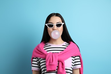 Photo of Fashionable young woman blowing bubblegum on light blue background