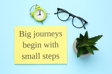 Motivational quote Big journeys begin with small steps, houseplant, glasses and alarm clock on light blue background, flat lay