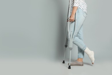 Woman with injured leg using crutches on grey background, closeup. Space for text