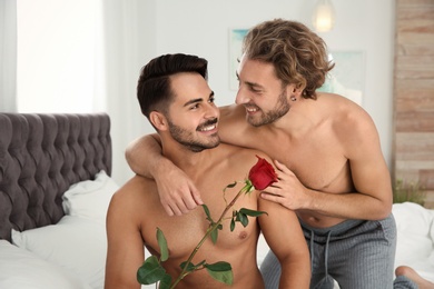 Happy gay couple with flower on bed at home