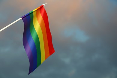 Bright rainbow LGBT flag against cloudy sky, space for text