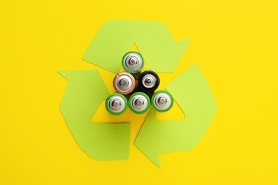 Used batteries and recycling symbol on yellow background, flat lay