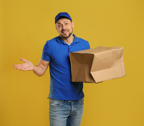 Emotional courier with damaged cardboard box on yellow background. Poor quality delivery service