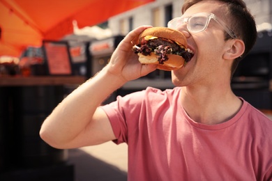 Photo of Young man eating burger in street cafe