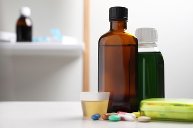 Photo of Bottles of syrup, measuring cup and pills on table, space for text. Cold medicine