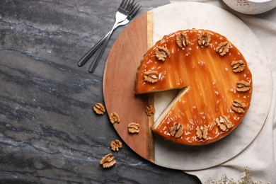 Delicious cheesecake with caramel and walnuts on black marble table, flat lay. Space for text